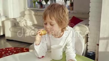 男孩在现代厨房吃早餐。 男孩吃带牛奶的饼干。 厨房里的白色桌子。 灰色碗在桌子上。